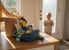 Parent packing a small travel sensory kit with quiet fidgets and kids earmuffs while a child holds a fidget, ready to head out