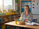 “Bright, playful primary school classroom scene with a teacher preparing a small basket of quiet sensory fidgets beside pencils and a lesson planner.