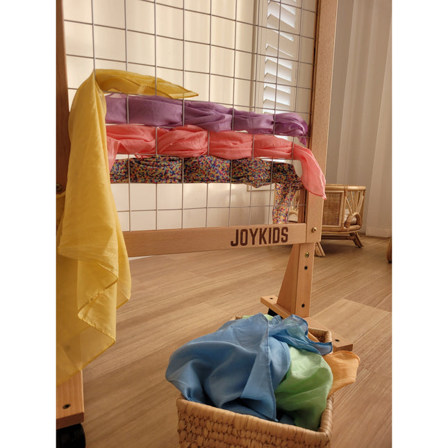 (NEW) Growth-Friendly Mobile Art Rack with colorful fabrics arranged and soft scarves in basket below, calm home setting