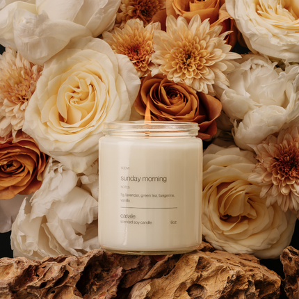 SUNDAY MORNING SINGLE WICKED SOY CANDLE (8oz / 226g) lit in front of soft cream and brown floral arrangement.