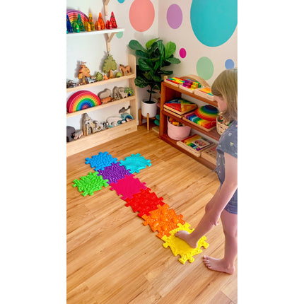 Child playing barefoot on colorful Rainbow Tactile Floor mat Set in a bright, organized sensory room