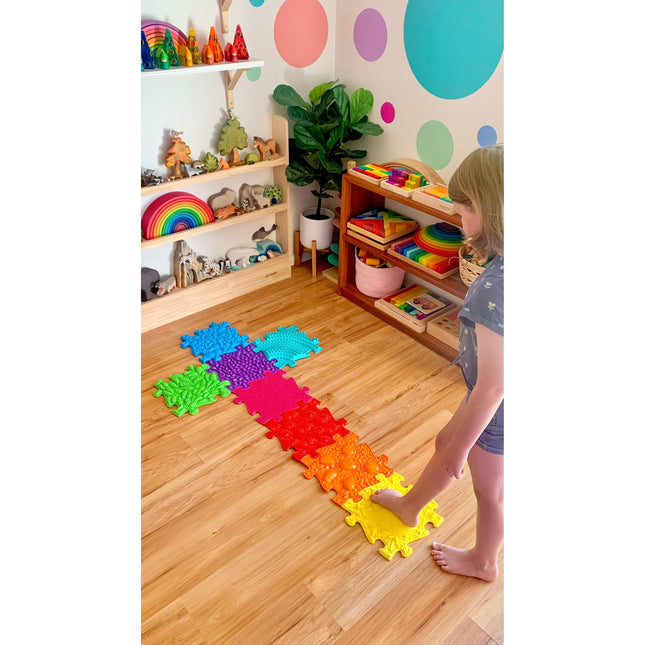 Child playing barefoot on colorful Rainbow Tactile Floor mat Set in a bright, organized sensory room