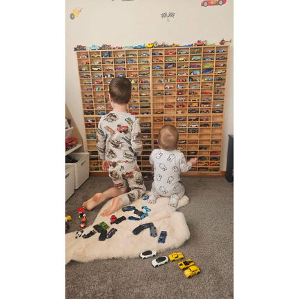 Two children playing with toy cars in front of a wooden JCAR 60 —Diecast Display Rack, helping families thrive with tools to calm, connect and support