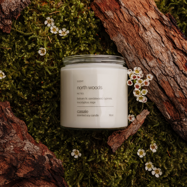 NORTH WOODS DOUBLE WICKED SOY CANDLE (16oz / 453g) on moss and bark with small white flowers, helping families thrive.