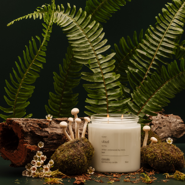 UBUD DOUBLE WICKED SOY CANDLE (16oz / 453g) lit with natural greenery, moss, and wood accents, calming sensory setup.