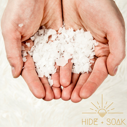 Hands holding white flakes bath salts with Hide + Soak logo, highlighting #1 Franki - Sports Recovery - Magnesium Flakes Bath Salts | 900g