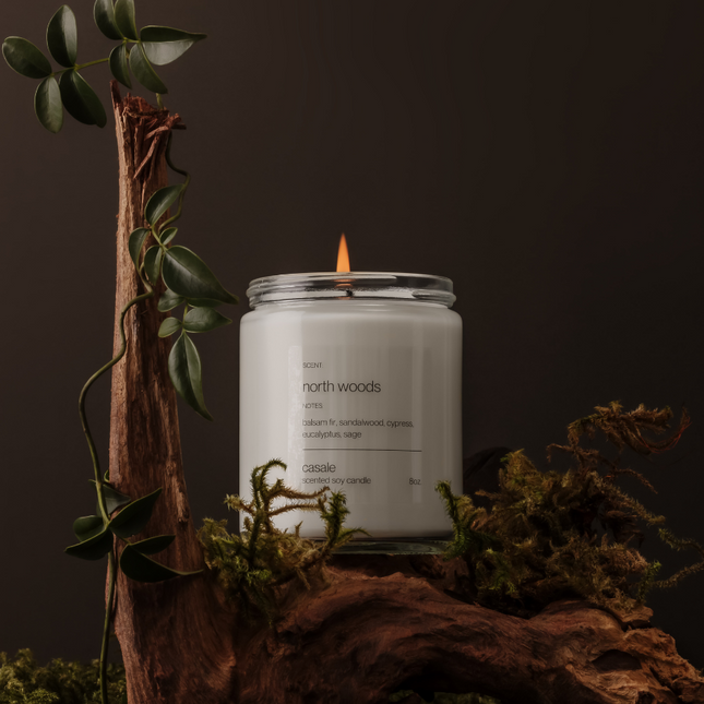 NORTH WOODS SINGLE WICKED SOY CANDLE (8oz / 226g) lit on natural wood with greenery, helping families thrive with tools to calm.