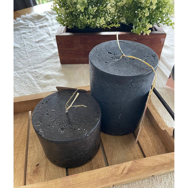 Charcoal Black Pillar Candle Stone Relic Finish with rustic texture placed on wooden tray near greenery, calming home decor.