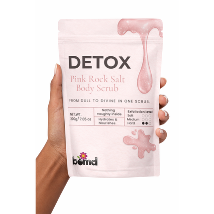 Hand holding a pouch of DETOX Pink Salt Scrub & Soak with soft pink design, promoting calm and support.