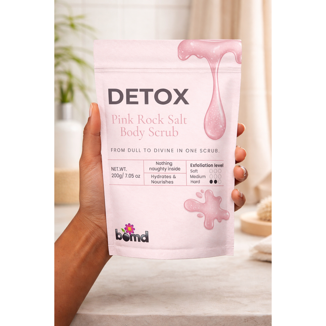 Hand holding DETOX Pink Salt Scrub & Soak package with pink design in bright bathroom setting