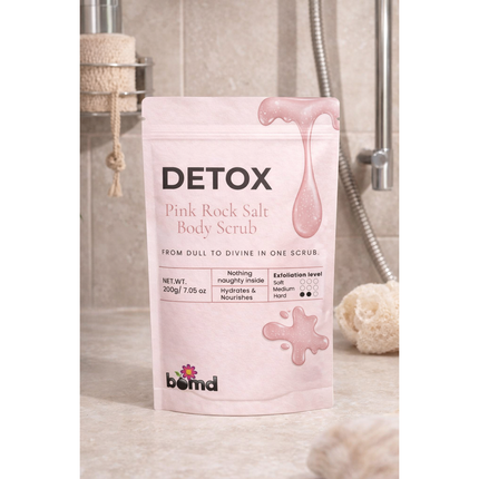 DETOX Pink Salt Scrub & Soak in pink packaging displayed in a bathroom setting with shower accessories.