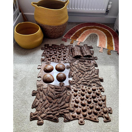 Muffik Eco Sensory Playmat - Individual with textured natural shapes on carpet next to woven baskets and rainbow rug.