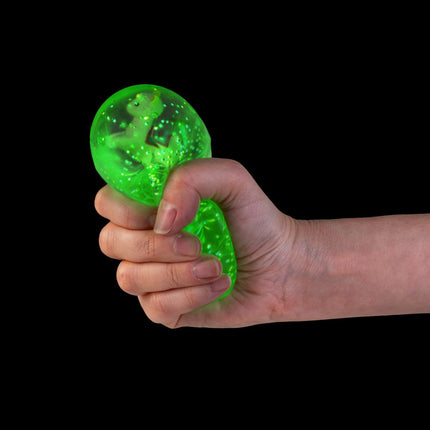 Hand squeezing a glowing green Smooshos Super Squeeze Diamond Sphere GID Alpaca sensory squishy toy against black background