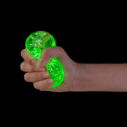Hand squeezing bright green glowing Smooshos Super Squeeze Diamond Sphere GID Koala sensory toy against black background