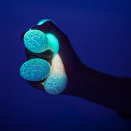 Hand gripping Smoosho's Glow-in-the-Dark Sticky Splat Ballz - Set of 3 glowing blue in dark background