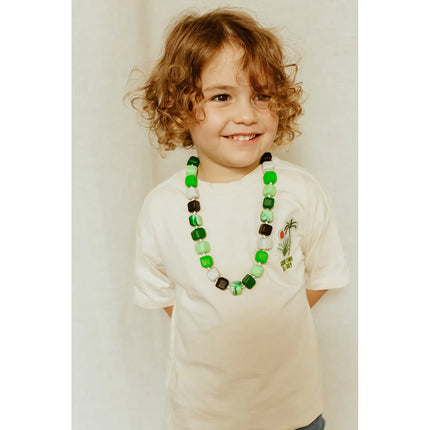 Young child smiling wearing a green and black beaded Princess & The Pea Necklace, helping families thrive with tools to calm.