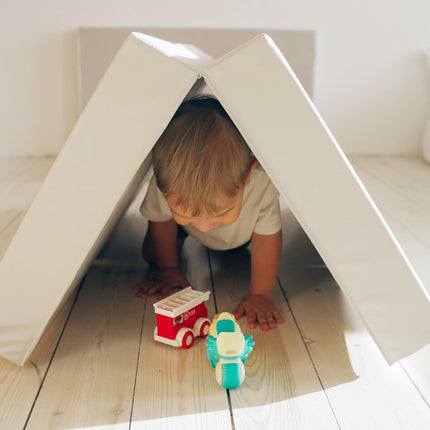 Child playing under grey soft cushions arranged as a tent on light wood floor with toy vehicles, Super Soft Foldable Landing Play Mats