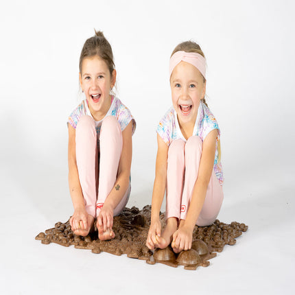 Two smiling girls sitting on a textured brown Muffik Eco Sensory Playmat - Individual, helping families thrive.