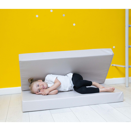 Child laying comfortably on light grey Super Soft Foldable Landing Play Mats against yellow wall indoors. Helping families thrive with tools to calm, connect and support.
