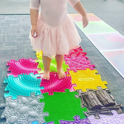 Child standing barefoot on colorful textured pieces of Large 2 Tactile Sensory floor mats set for sensory play.