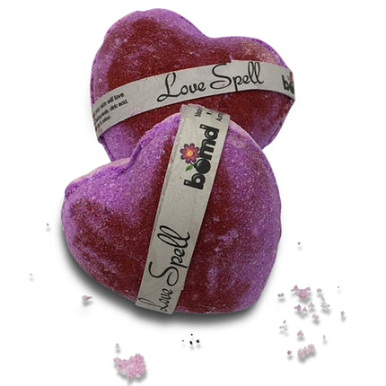Two heart-shaped bath bombs in purple shades with labels, part of Love Spell Bubble Bath Bomb with a Little Shimmer Set of 6.