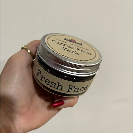 Hand holding Fresh face Coffee Scrub Face Mask - Lightly Exfoliating Face Masque jar with beige label, helping families thrive.