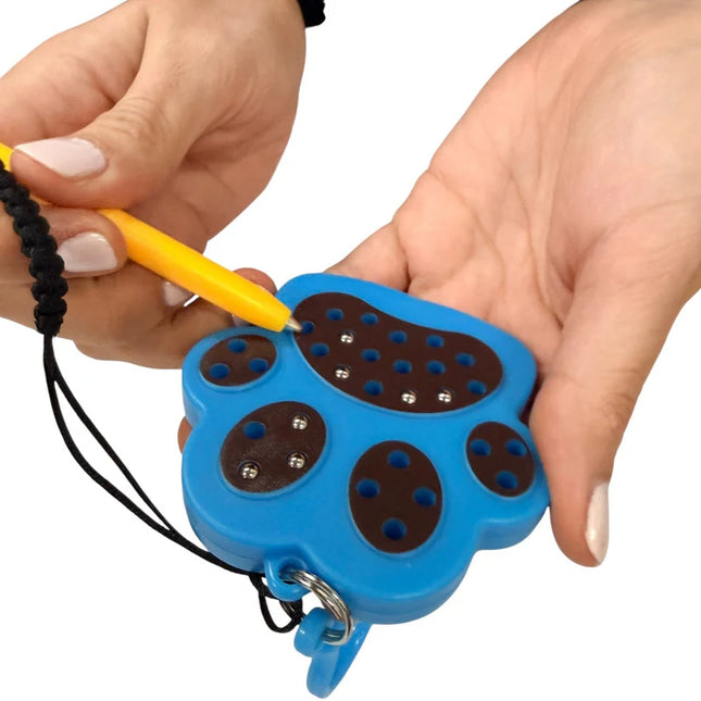 Person holding a blue and brown Paw Magnetic Pad Keyring with metal balls and using a yellow stylus to move the balls inside the paw-shaped sensory toy.