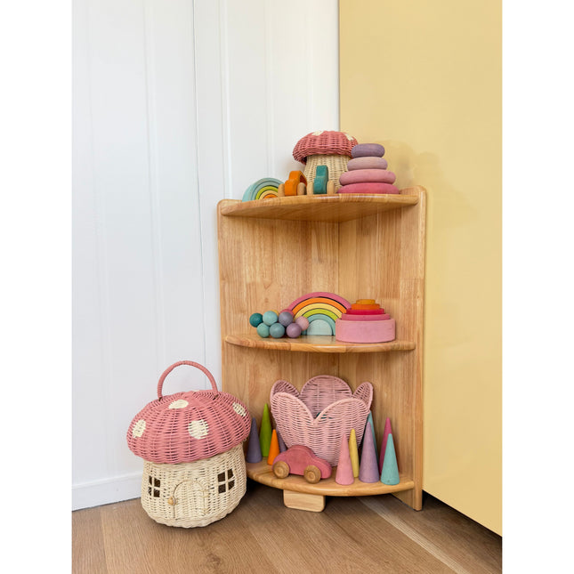 JORA Corner 3-Tier Corner Shelf holding colorful wooden toys and wicker baskets against white and yellow walls.
