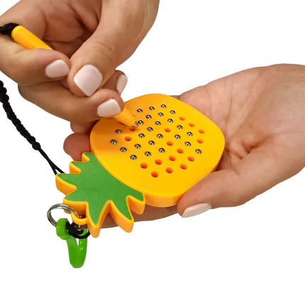Person using a yellow pen on a Pineapple Magnetic Pad Keyring with metallic balls and green pineapple leaf detail attached to a black lanyard and green clip.