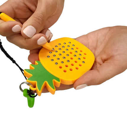 Person holding and using a yellow Pineapple Magnetic Pad Keyring with a small magnetic stylus to activate metal balls on the pad, designed as a sensory toy and keychain accessory.
