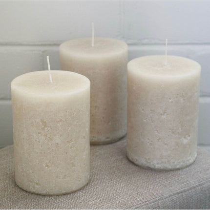 Three off white pillar candles with rustic relic design on a fabric surface, helping families thrive with tools to calm connect and support