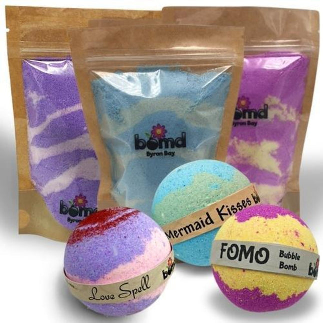 Three colorful bath bombs and matching fizzy dust in resealable brown pouches, Bubble Bath Fizzy Dust & Bubble Bomb set Mermaid Kisses Love Spell FOMO helping families thrive.