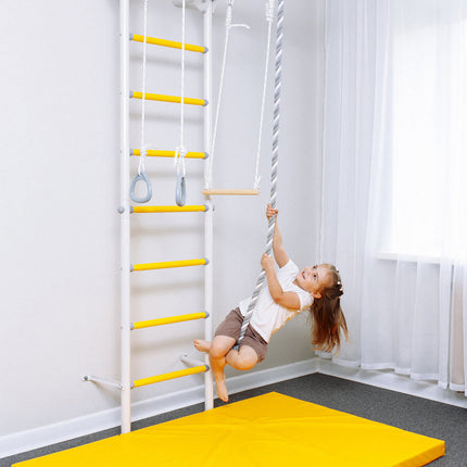 Child playing on Sensory Swedish Wall Bars with yellow rungs, rings, rope swing, and padded mat below.