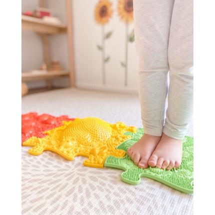 Child standing barefoot on colorful textured puzzle pieces of Rainbow Tactile Floor mat Set, sensory play and support.