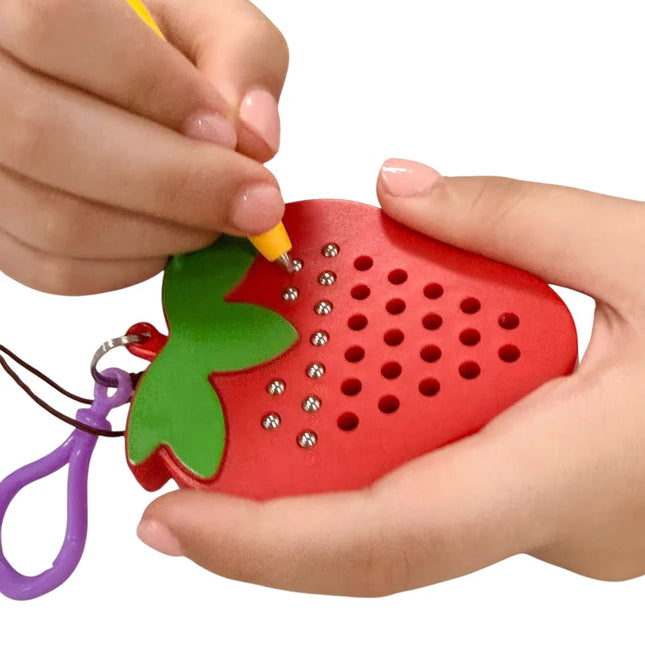 Hands holding and interacting with a red and green sensory toy shaped like a strawberry with metal balls, identified as Strawberry Magnetic Pad Keyring.
