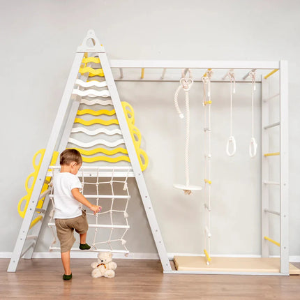 Child playing on a white and yellow Wooden Teepee Playground with climbing net and hanging rings in a sensory-friendly space