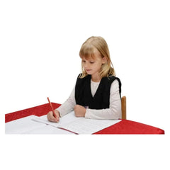 Child wearing Weighted Shoulder Wraps focused on writing at a table, helping families thrive with tools to calm and support.