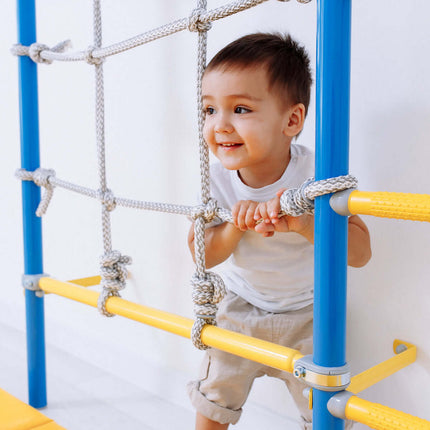 Young child playing on Swedish Giant Wallbars - S7 with blue and yellow frame and rope net sensory play gym