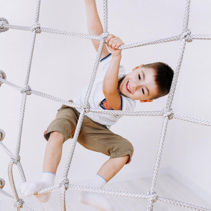Child smiling and climbing rope net on Swedish Home Play gym set - No Drill, helping families thrive with tools to calm connect and support