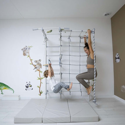 Child and adult playing on Swedish Giant Wallbars - S7 indoor climbing frame with mats below in a playroom