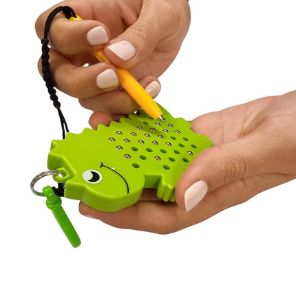 Close-up of hands holding a green dinosaur-shaped Dinosaur Magnetic Pad Keyring with a yellow magnetic stylus for tracing patterns.