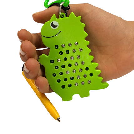 Hand holding a green dinosaur-shaped Dinosaur Magnetic Pad Keyring with small silver magnetic balls and attached yellow stylus pen.