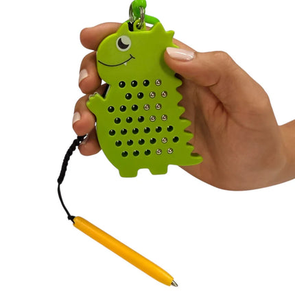 Hand holding a green dinosaur-shaped magnetic toy with small metal balls and a yellow stylus attached, called Dinosaur Magnetic Pad Keyring.
