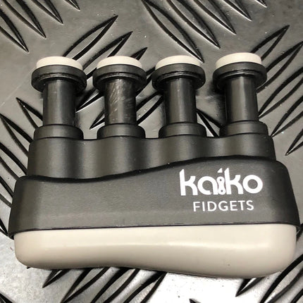 Black and gray Hand & Finger Grip Exerciser & Fidgeting Sensory Tool with four finger buttons on a textured surface background.