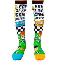 Game Socks with colorful graphics saying Eat Sleep Game Repeat and playful soccer cartoon characters on green background.