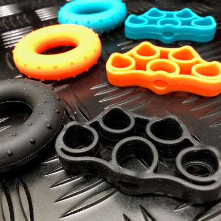 Close-up of colorful silicone grip stretch bands and stress rings in blue, orange, and black on a textured surface, showing the Stretch Bands & Stress Rings - Boxed Set of 6.