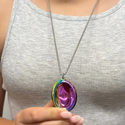 Person wearing a Groove Stone - Dual Support Necklace & Key Chain with colorful metallic pendant held in hand against a gray top.