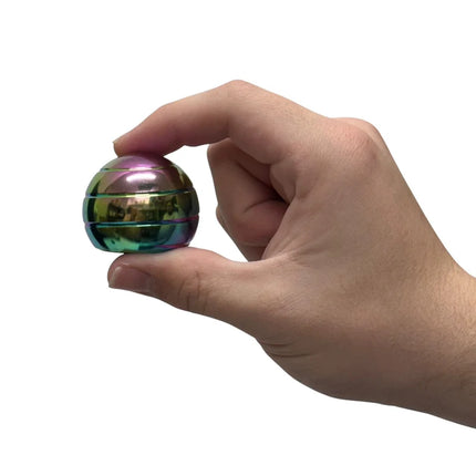 Hand holding a small shiny metal toy with rainbow colors called Gyroscope - 70gm against a white background.