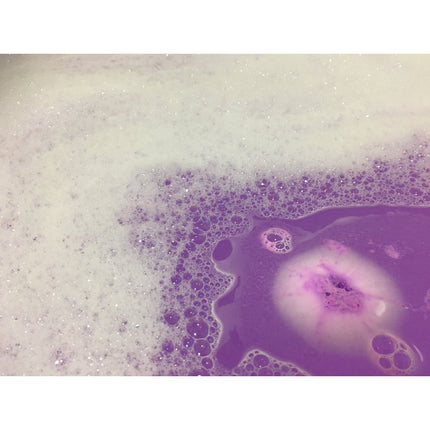 Love Spell Bubble Bath Bomb with Glitter dissolving in water creating purple foam and sparkling bubbles.