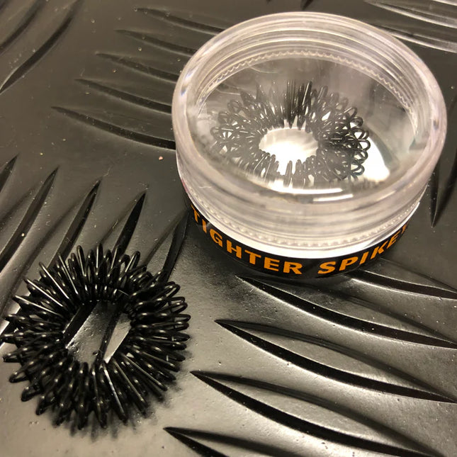 Standard Finger Spikey black sensory ring with flexible spikes beside clear plastic container on textured surface